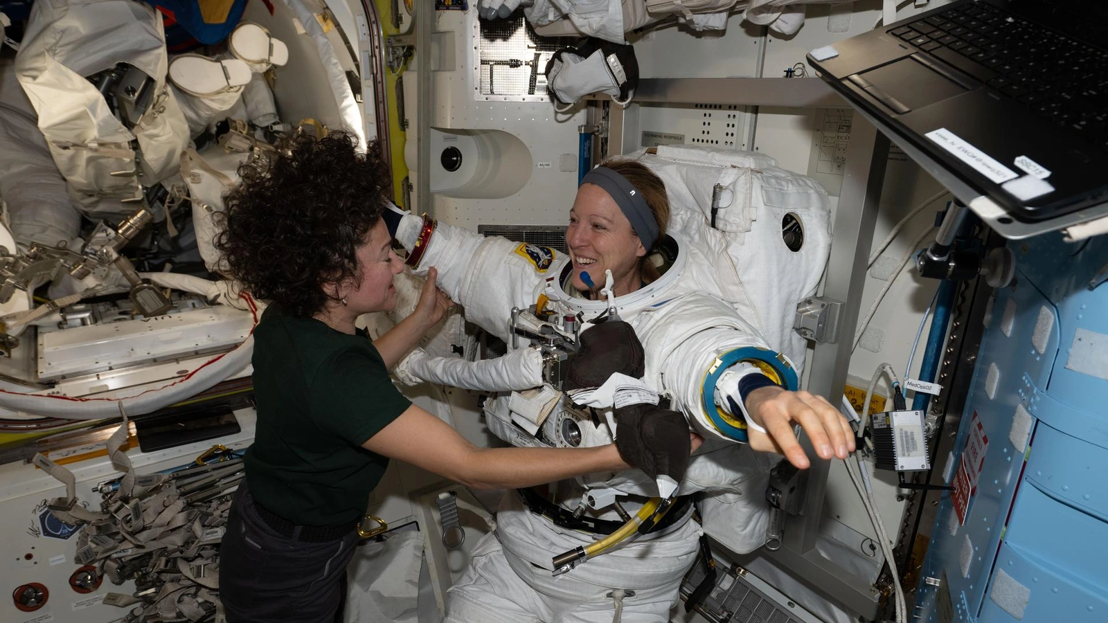 NASA photograph of a suited astronaut being assisted inside the International Space Station's Quest airlock during preparation for a planned maintenance spacewalk; it is contextual and not the retroreflector worksite